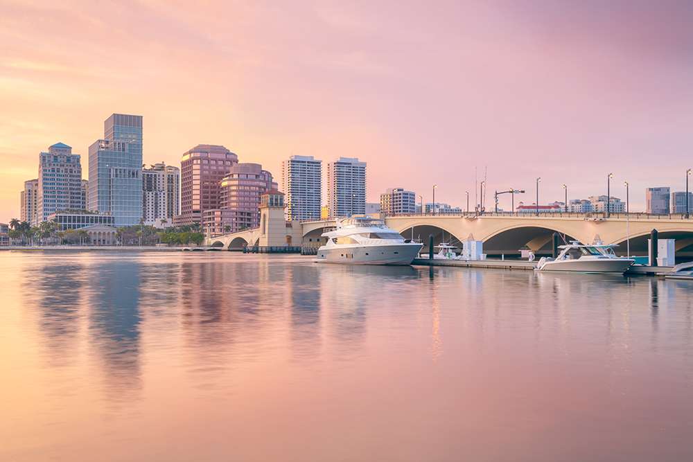Cityscape image of West Palm Beach, Florida with reflection of the city skyline in the water at beautiful sunset.